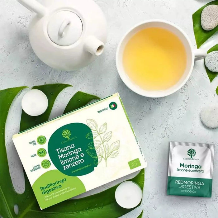 Tisana Moringa, limone e zenzero RedMoringa con teiera, tazza di infuso e bustina filtro su foglie verdi